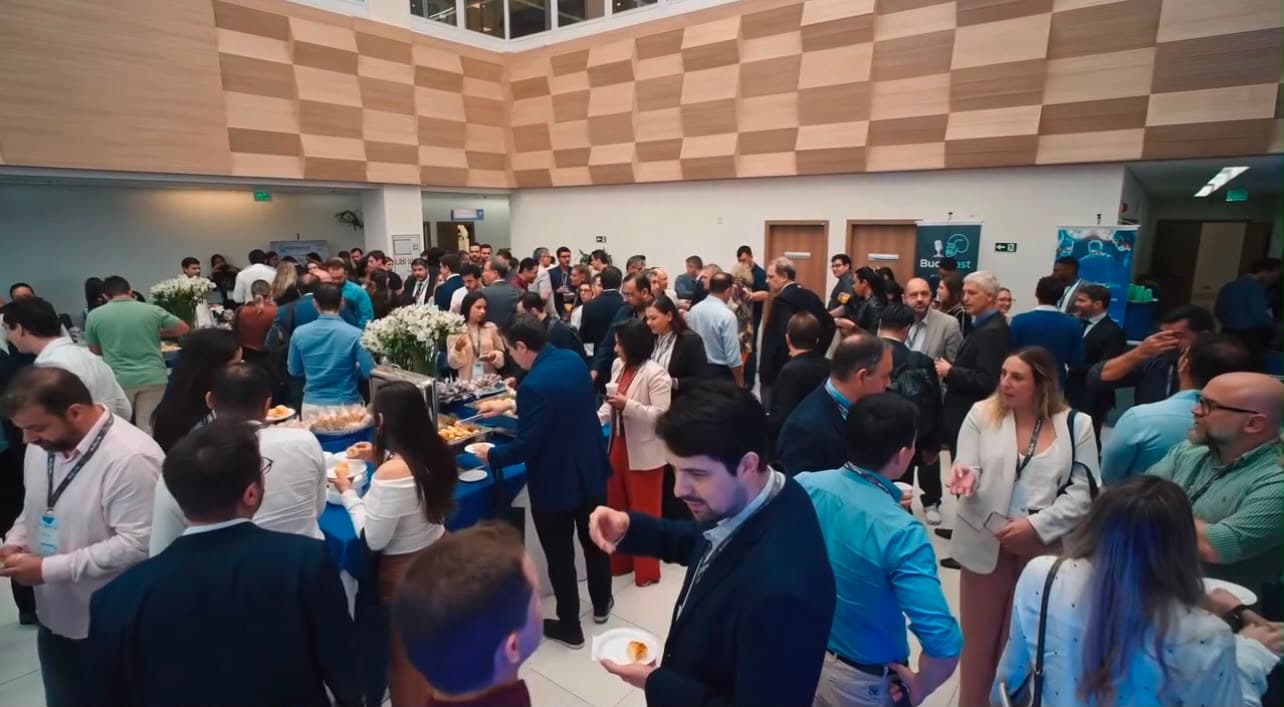 Vista ampla do foyer com participantes servindo-se no coffee break
