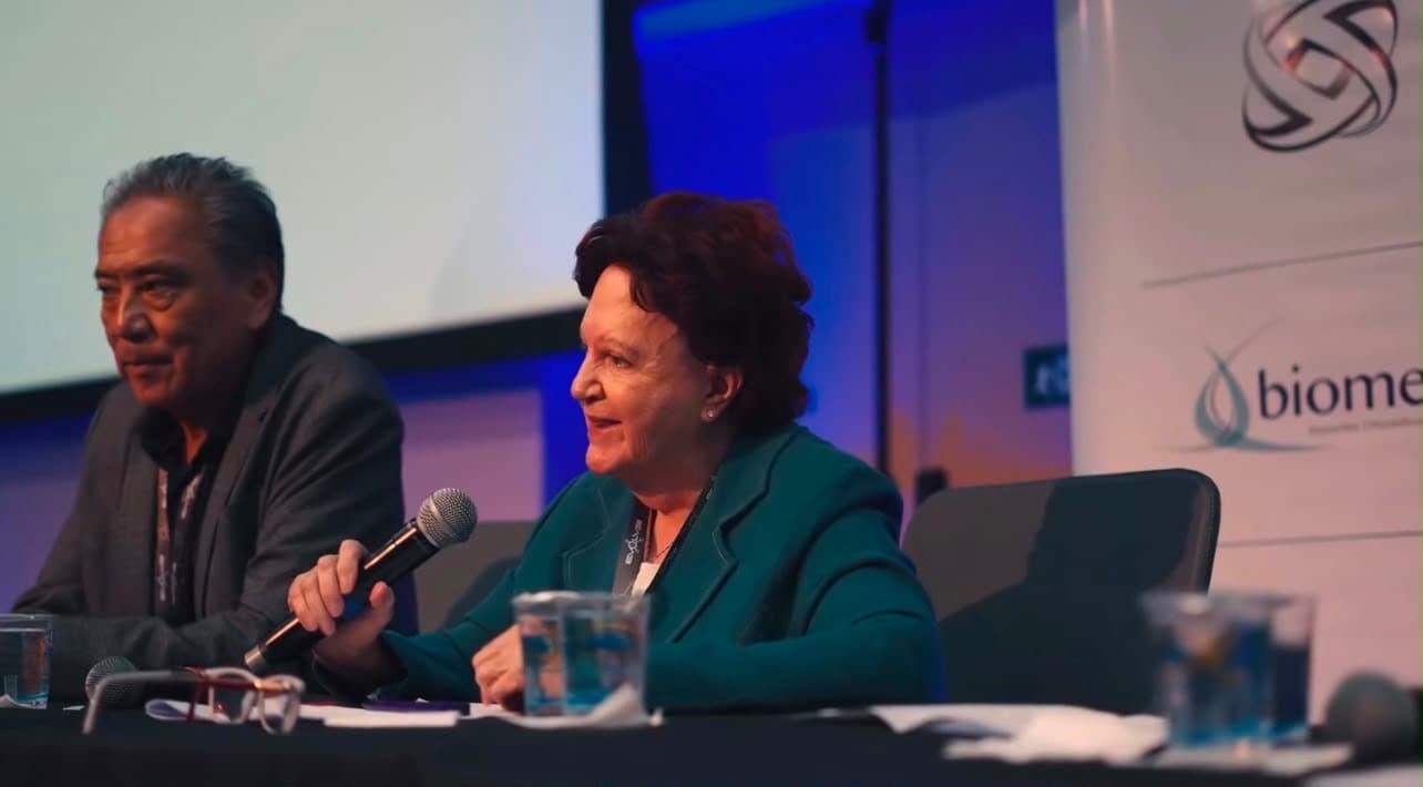 Palestrante ao microfone na mesa de debate, ao lado de outro especialista